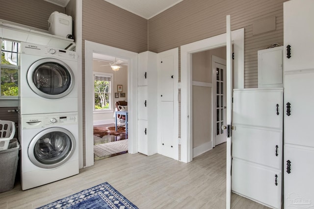 laundry room featuring light wood finished floors, a ceiling fan, stacked washing maching and dryer, and laundry area