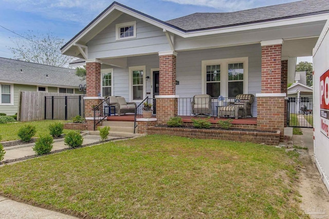 craftsman house featuring a porch, brick siding, fence, roof with shingles, and a front yard