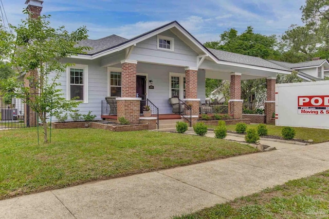 craftsman-style house with covered porch, a front yard, central air condition unit, fence, and brick siding