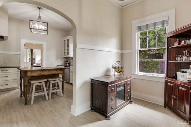bar featuring arched walkways, a chandelier, range, light wood-style floors, and baseboards