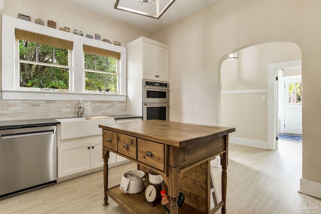 kitchen featuring a sink, a wealth of natural light, backsplash, arched walkways, and appliances with stainless steel finishes