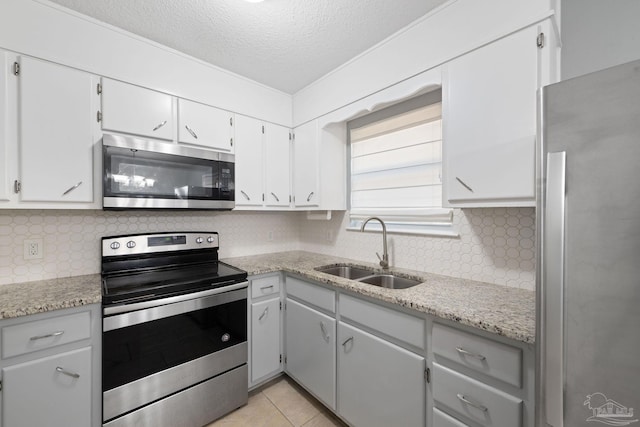 kitchen with light tile patterned floors, stainless steel appliances, tasteful backsplash, a sink, and a textured ceiling