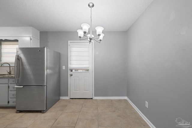 kitchen with baseboards, a sink, freestanding refrigerator, and an inviting chandelier