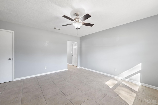 tiled empty room featuring a ceiling fan, visible vents, a textured ceiling, and baseboards