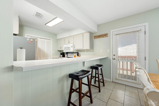 8425 Gulf Blvd Unit 213, Navarre Beach, FL 32566 - kitchen featuring freestanding refrigerator, white microwave, light countertops, white cabinets, and a kitchen breakfast bar