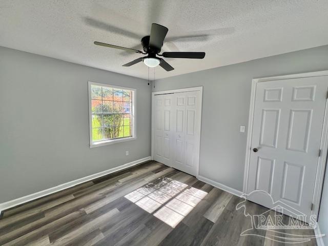 unfurnished bedroom featuring ceiling fan, a closet, dark wood-type flooring, and a textured ceiling