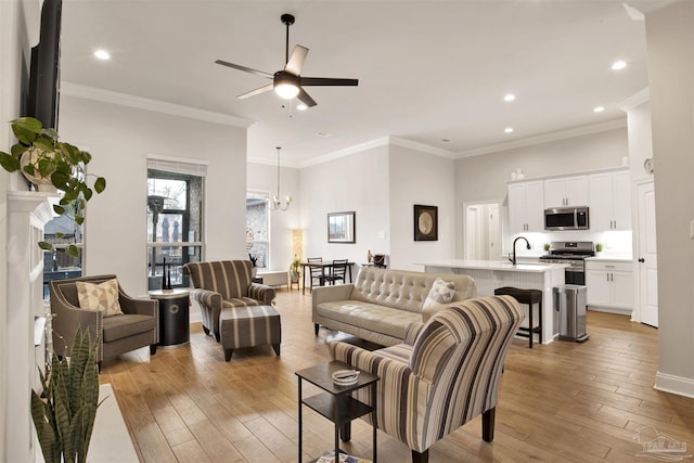 living room featuring ornamental molding, sink, ceiling fan with notable chandelier, and light wood-type flooring