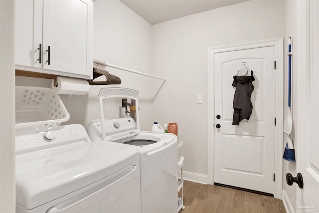 clothes washing area with washer and clothes dryer, cabinets, and light wood-type flooring