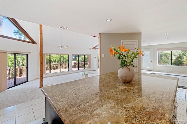 kitchen with a breakfast bar area, light stone countertops, a center island, light colored carpet, and ceiling fan