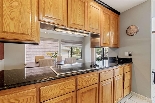 kitchen with kitchen peninsula, dark stone countertops, light tile patterned floors, and stovetop