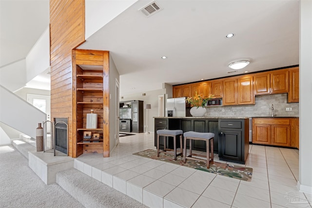 kitchen with tasteful backsplash, light tile patterned flooring, a kitchen bar, a center island, and stainless steel fridge