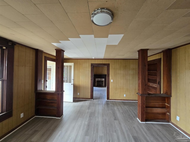 spare room featuring a fireplace, hardwood / wood-style floors, ornate columns, and wood walls