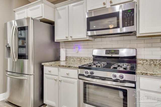 kitchen featuring light stone counters, appliances with stainless steel finishes, white cabinets, and decorative backsplash