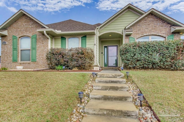 single story home featuring roof with shingles, a front yard, and brick siding