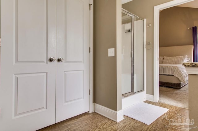 full bathroom featuring a shower stall, baseboards, connected bathroom, and wood finished floors