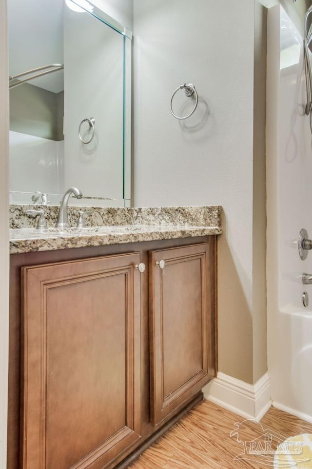 full bath featuring a shower, vanity, baseboards, and wood finished floors