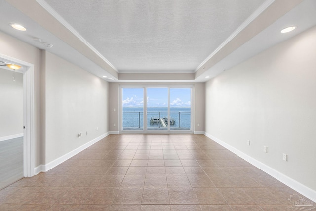 tiled spare room with a textured ceiling, a water view, crown molding, and a tray ceiling