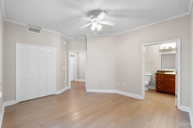 unfurnished bedroom with ceiling fan, ensuite bathroom, a textured ceiling, and light wood-type flooring