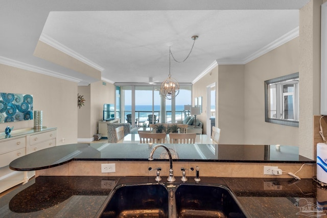 kitchen featuring pendant lighting, sink, dark stone countertops, a notable chandelier, and ornamental molding