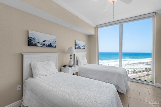 tiled bedroom with a water view, ceiling fan, floor to ceiling windows, and a view of the beach