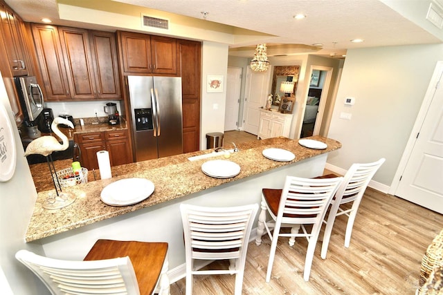 645 Lost Key Dr Unit 406D, Perdido Key, FL 32507 - kitchen featuring a kitchen breakfast bar, stainless steel fridge with ice dispenser, visible vents, light stone countertops, and light wood-style flooring