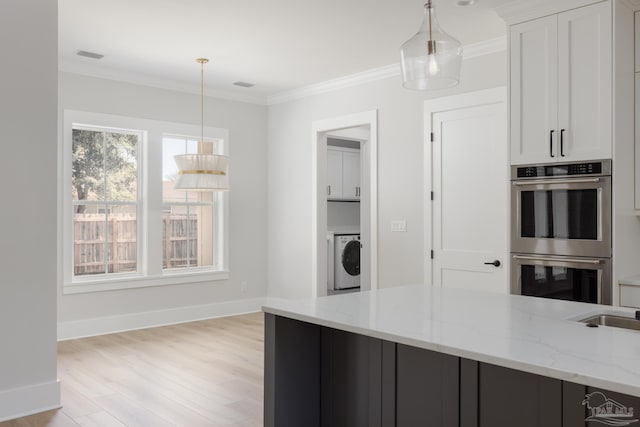 kitchen featuring light stone counters, ornamental molding, pendant lighting, stainless steel double oven, and washer / clothes dryer