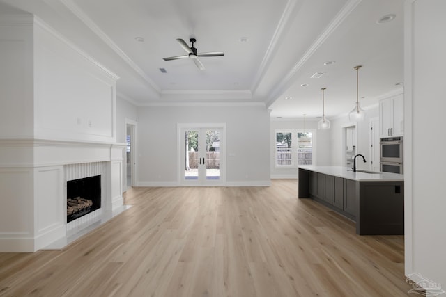 unfurnished living room featuring a tray ceiling, sink, ceiling fan, light hardwood / wood-style floors, and crown molding