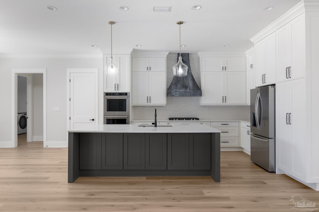 kitchen with sink, premium range hood, appliances with stainless steel finishes, hanging light fixtures, and white cabinets