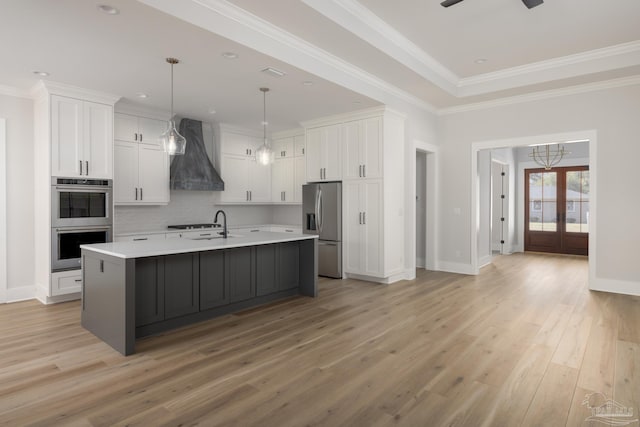 kitchen with premium range hood, decorative light fixtures, appliances with stainless steel finishes, a kitchen island with sink, and white cabinets