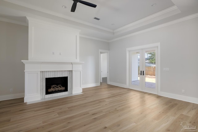 unfurnished living room featuring french doors, crown molding, a tray ceiling, a fireplace, and light hardwood / wood-style floors