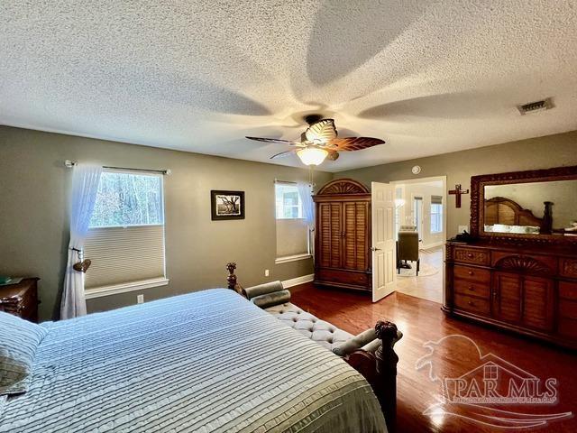 bedroom with a ceiling fan, a textured ceiling, visible vents, and wood finished floors