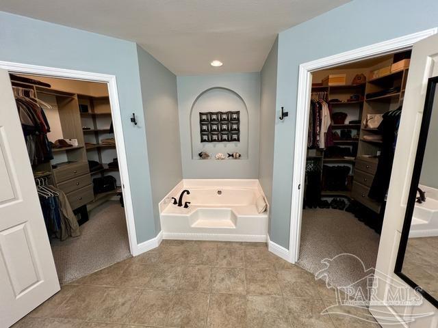 bathroom featuring tile patterned flooring, a walk in closet, a bath, and baseboards