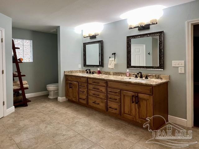 full bath featuring double vanity, baseboards, toilet, and a sink