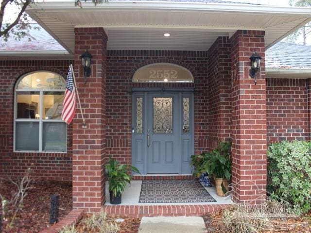 entrance to property with a shingled roof and brick siding