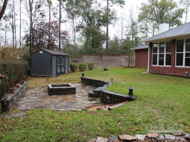 view of yard featuring a fire pit, a patio, fence, an outdoor structure, and a shed