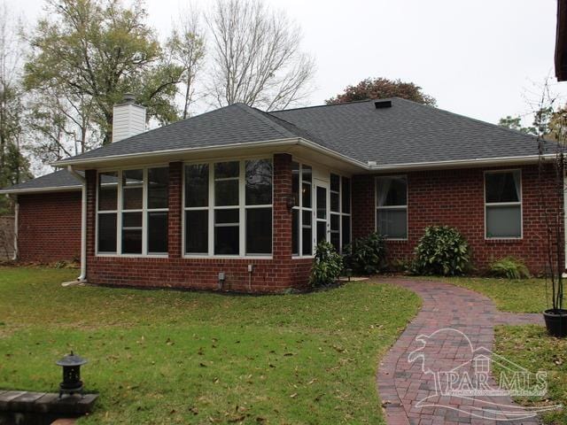 back of property with a yard, roof with shingles, a chimney, and brick siding