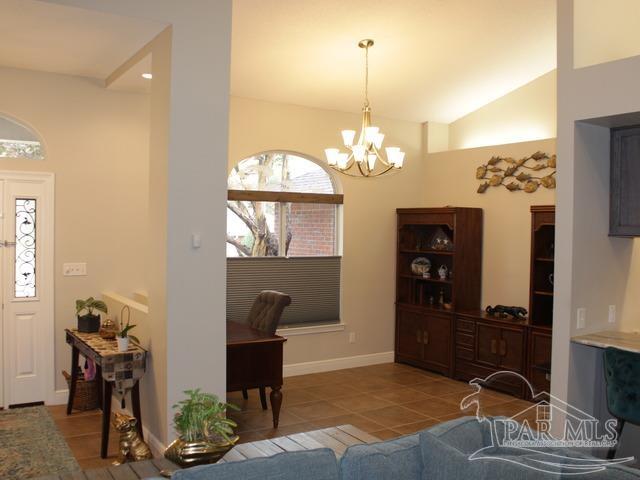 tiled living room with a chandelier, vaulted ceiling, and baseboards