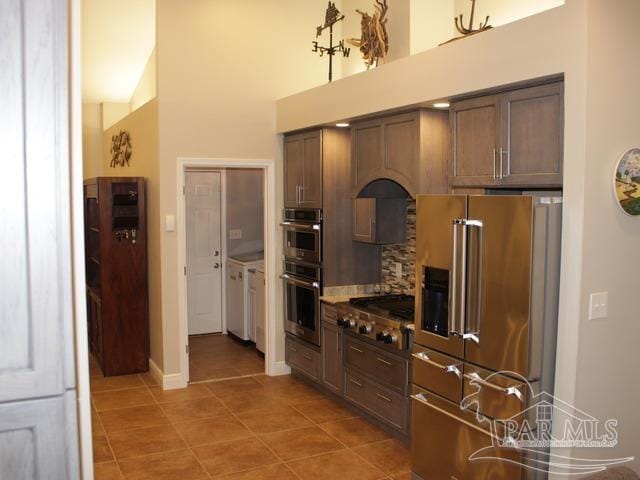 kitchen with stainless steel appliances, backsplash, a high ceiling, light tile patterned flooring, and baseboards