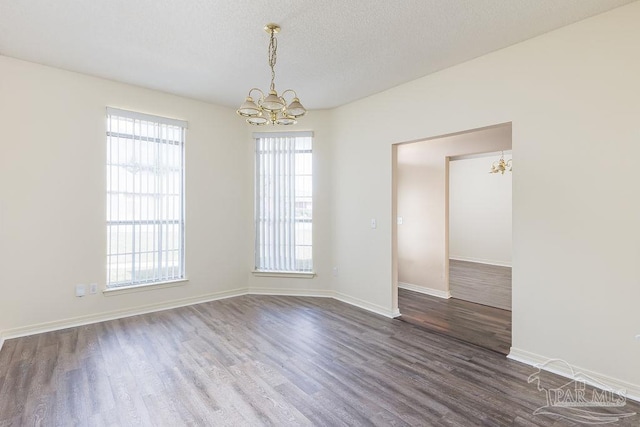 unfurnished room with an inviting chandelier, dark hardwood / wood-style flooring, a wealth of natural light, and a textured ceiling