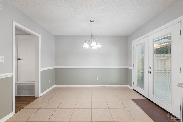 unfurnished dining area featuring french doors, a textured ceiling, a notable chandelier, and light tile patterned flooring