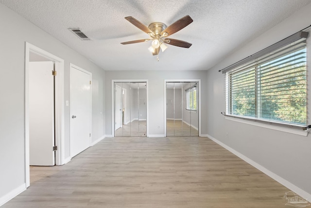 unfurnished bedroom with multiple closets, ceiling fan, a textured ceiling, and light wood-type flooring