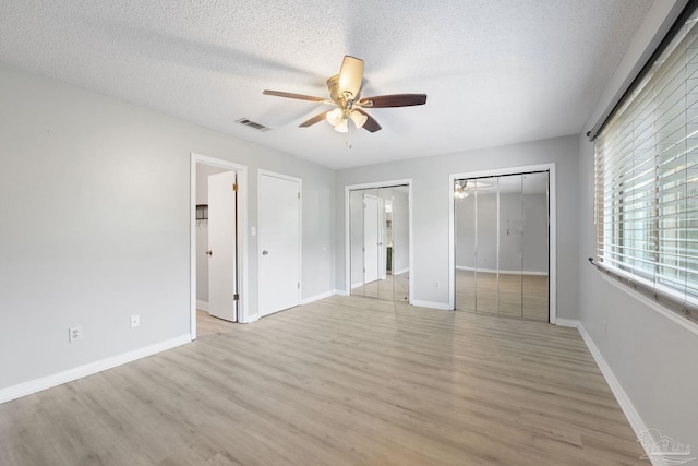 unfurnished bedroom with ceiling fan, light wood-type flooring, a textured ceiling, and two closets