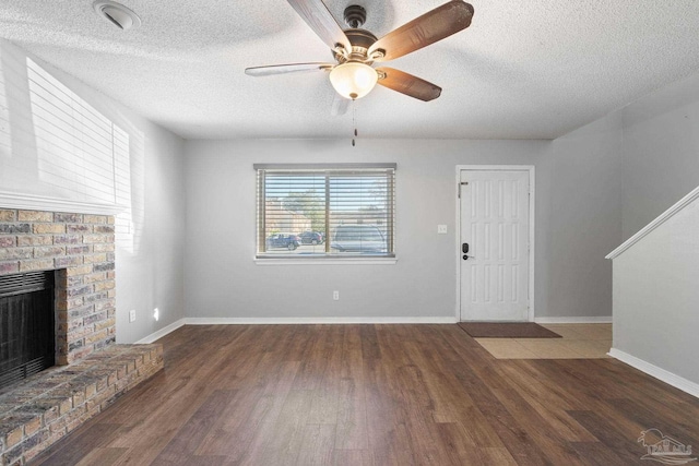 unfurnished living room featuring ceiling fan, a fireplace, dark wood-type flooring, and a textured ceiling