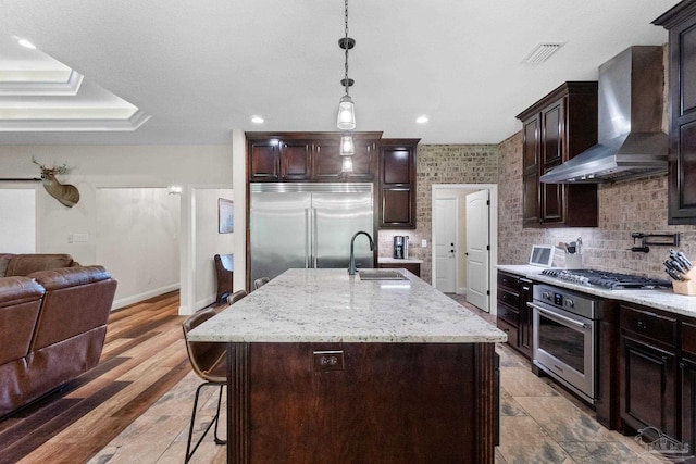 kitchen with a sink, open floor plan, visible vents, wall chimney range hood, and appliances with stainless steel finishes