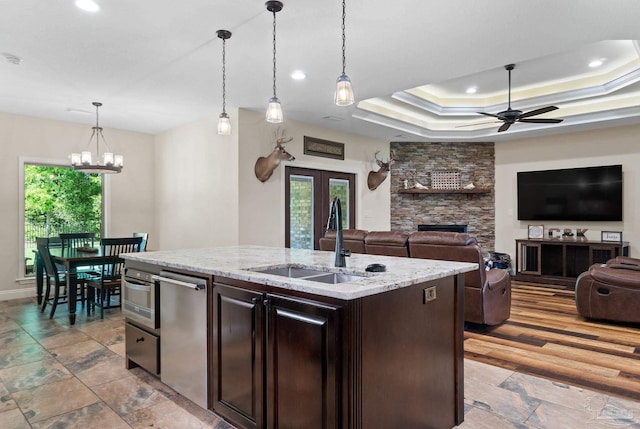 kitchen featuring dark brown cabinets, a stone fireplace, a sink, ceiling fan with notable chandelier, and decorative light fixtures