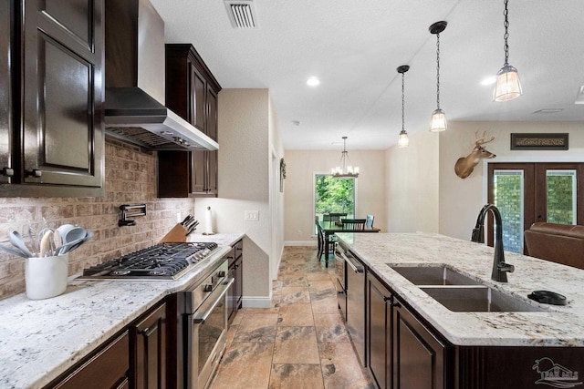 kitchen with visible vents, a sink, wall chimney exhaust hood, baseboards, and tasteful backsplash
