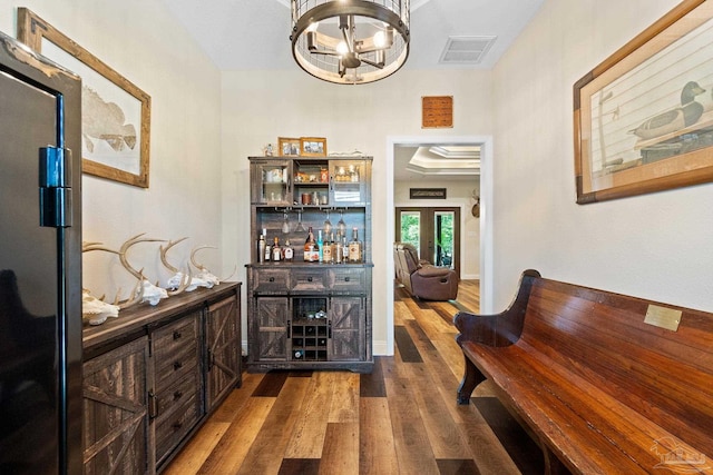 interior space with an inviting chandelier, visible vents, a bar, freestanding refrigerator, and dark wood-style flooring