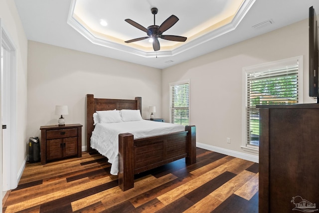 bedroom with a ceiling fan, wood finished floors, a tray ceiling, baseboards, and visible vents
