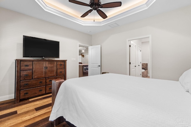 bedroom with a raised ceiling, wood finished floors, visible vents, baseboards, and ceiling fan