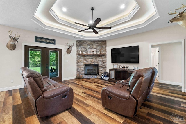 living room featuring a raised ceiling, wood finished floors, crown molding, a fireplace, and ceiling fan